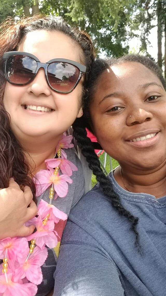 Two ladies standing in a park, with a tree behind them. Both ladies are smiling.