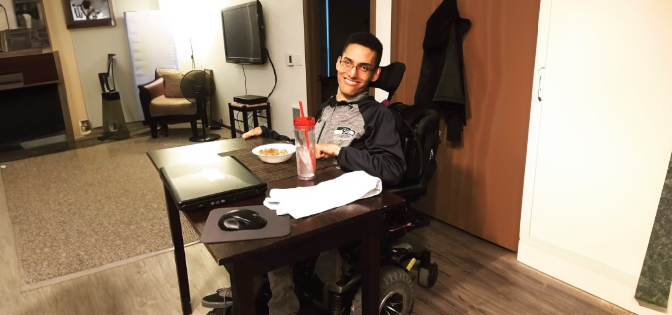 A man in a power wheelchair sitting at a table with dinner laid out in front of him.